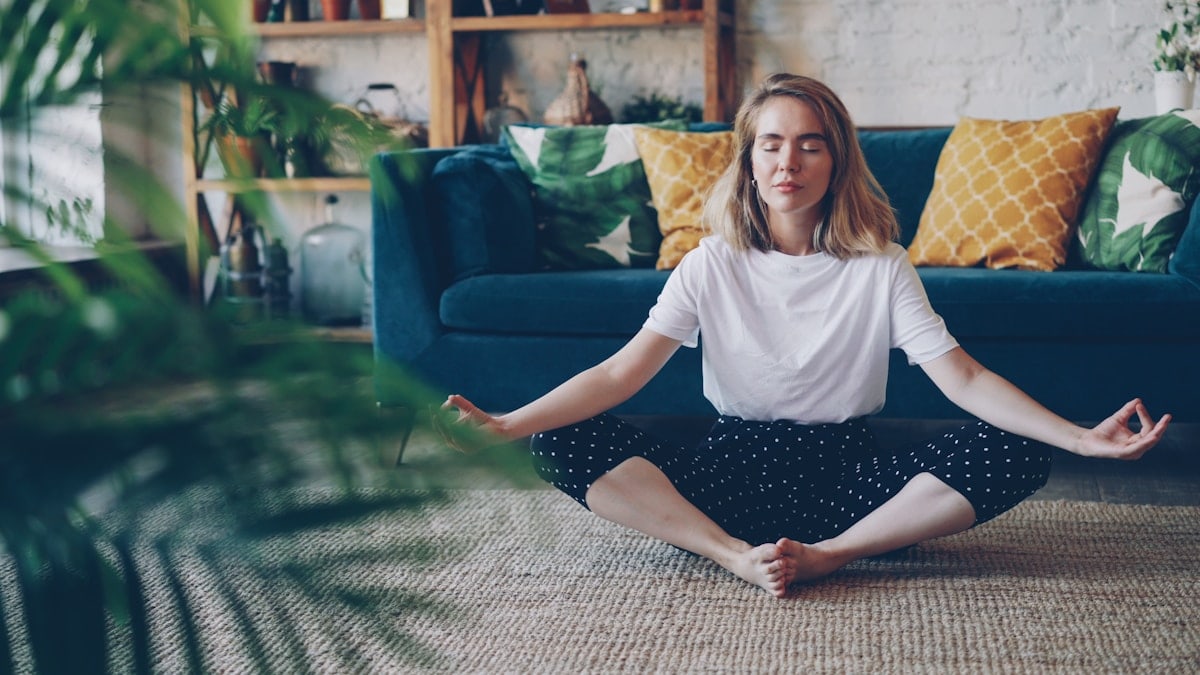 Flexible young lady is relaxing in Badha Konasana position practising Butterfly yoga pose at home enjoying rest and relaxation. Wellbeing, interior and people concept.